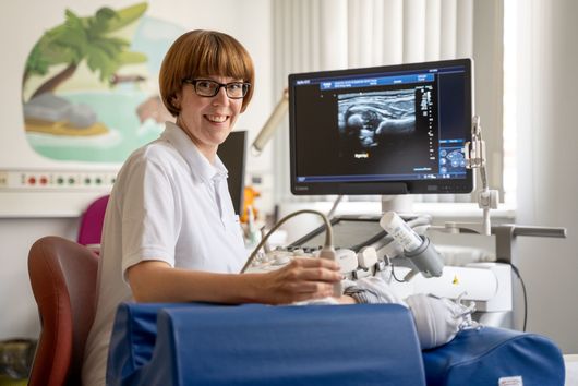 Eine Frau untersucht ein Baby auf einer Liege.