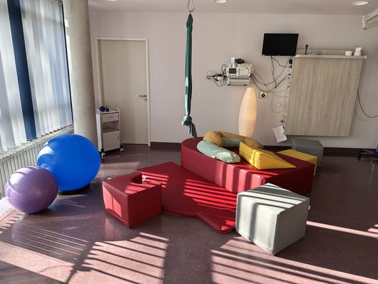 In einem Kreißsaal liegen Weiche Matten, modulare Schaumstoffelemente, Gebärhocker, Geburtstücher, Pezzibälle und gemütliche Sitzgelegenheiten, die eine aktive, selbstbestimmte Geburt fördern.