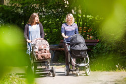 Zwei Mütter gehen mit ihren Neugeborenen im Kinderwagen spazieren.