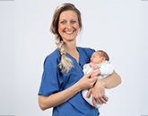 Hebamme hält ein Baby im Arm.