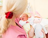 Hebamme hält Baby und Kuschelhasen im Arm.