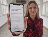 Frau zeigt Handy mit geöffneter Patienten-App.