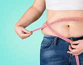 Eine Person mit Adipositas hält ein Maßband um ihren Bauch.