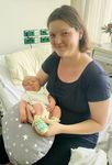 Eine Frau lächelt in die Kamera und hält ein Baby im Arm.